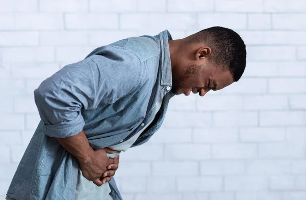 Homem negro sofrendo de dor de estômago em pé sobre a parede branca, vista lateral — Fotografia de Stock