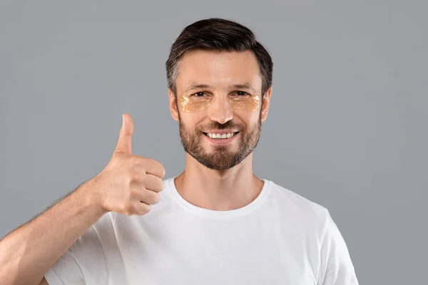 Middle-aged man with golden patches under eyes showing thumb up — Stock Photo, Image