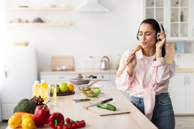Tasasız genç kadın mutfakta şarkı söyleyip dans ediyor.