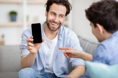 Modern teknoloji konsepti. Babası, oğluna siyah ekranlı akıllı telefonu gösteriyor. Telefonu da modelleme yeri.