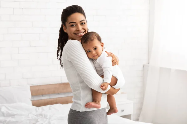 Afro-Amerikaanse mama dragen kleine baby staande in slaapkamer Indoor — Stockfoto
