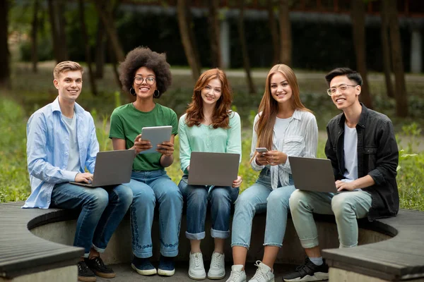 Les meilleurs gadgets pour les étudiants. Les adolescents multiraciaux assis avec des appareils électroniques sur le campus — Photo