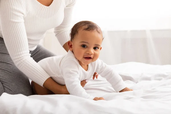 Unrecognizable Black Mom Helping Baby Son Crawl In Bedroom, Cropped