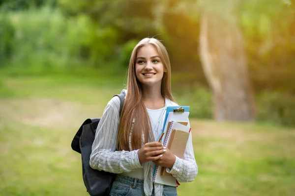 Девушка-первокурсница. Красивая студентка колледжа с учебниками и рюкзаком позирует на открытом воздухе — стоковое фото