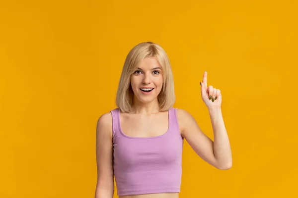 Έννοια έμπνευσης. Ενθουσιασμένη γυναίκα υψώνει το δάχτυλο και χαμογελά, έχοντας wow δημιουργική ιδέα πάνω από κίτρινο φόντο στούντιο — Φωτογραφία Αρχείου