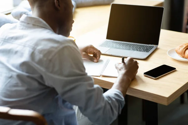 Felismerhetetlen fekete srác használja laptop üres képernyőn, online tanul, jegyzetel a kávézóban, mockup a design — Stock Fotó