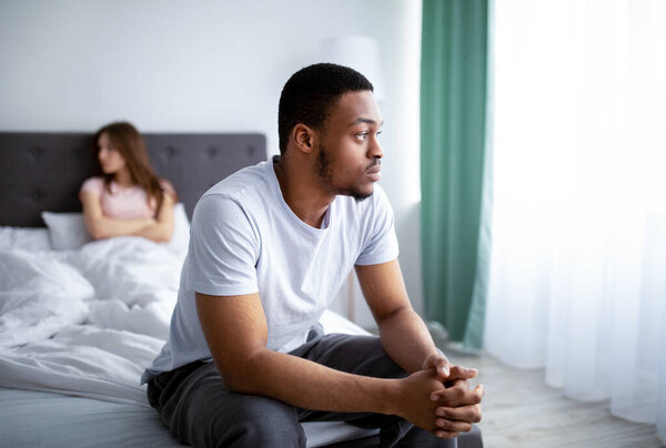 Кризис отношений. Молодой чернокожий мужчина расстраивается после ссоры с женой, сидит на кровати дома
