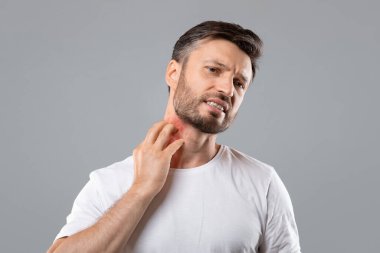 Bearded man scratching neck on grey background, having annoying itch clipart