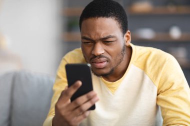 Afrikalı Amerikalı adam cep telefonu kullanırken gözlerini kısıyor.