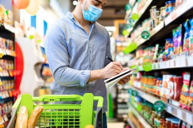 Alışveriş listesine not alan adam süpermarketten yiyecek alıyor.