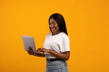 Gülümseyen siyah kadın dizüstü bilgisayarını sarıda tutuyor.