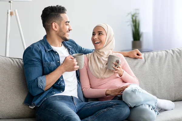 Fröhliches arabisches Paar posiert auf Sofa und hält Becher mit Getränken in der Hand — Stockfoto