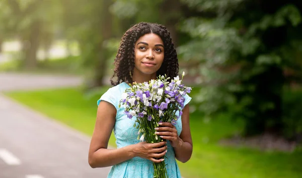 Parkta bir buket çiçekle romantik elbiseli hayalperest zenci kız. — Stok fotoğraf