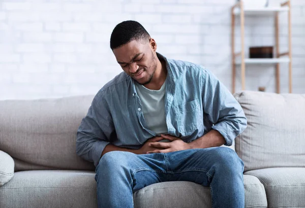 Negro chico having doloroso estomachache tocando aguijón estómago sentado en interior — Foto de Stock