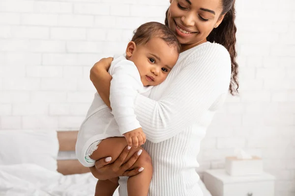 Африканская мамочка обнимает маленького сына, неся его в руках в помещении — стоковое фото
