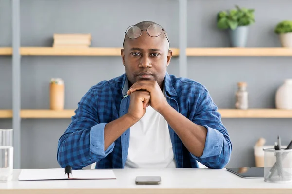 Retrato de un hombre de negocios afroamericano serio mirando la cámara mientras está sentado en casa en el lugar de trabajo — Foto de Stock
