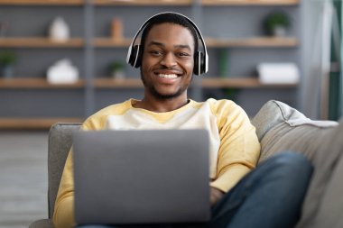 Kanepede yatıp dizüstü bilgisayarda film izleyen neşeli siyahi adam.