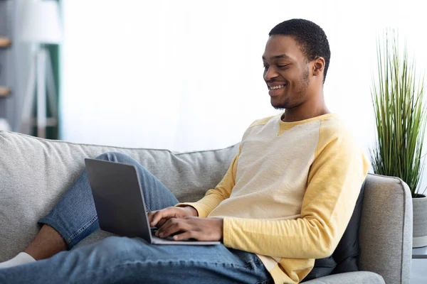 Χαλαρωμένος μαύρος τύπος που χρησιμοποιεί φορητό υπολογιστή στο σπίτι — Φωτογραφία Αρχείου
