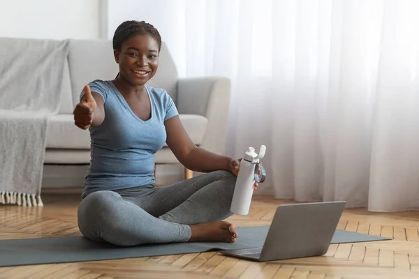 Черная женщина тренирует спорт с ноутбуком дома и показывает большой палец вверх — стоковое фото