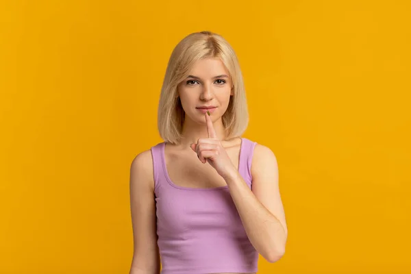 Shh, het is een geheim. Vrouw gebaart zwijgteken, legt vinger op lippen, maakt stille gebaar op gele achtergrond — Stockfoto