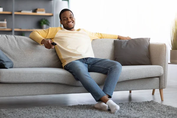 Χαλαρωμένος Αφροαμερικάνος που ανοίγει κανάλια στην τηλεόραση. — Φωτογραφία Αρχείου