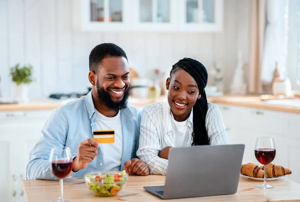 Lebensmittelbestellung. Glückliche schwarze Ehepartner mit Laptop und Karte in der Küche — Stockfoto