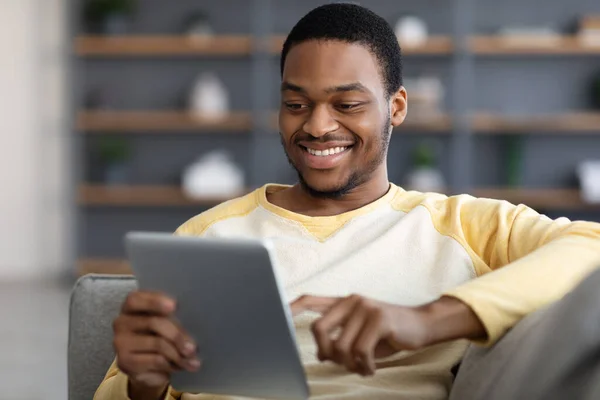 Positieve zwarte man liggend op de bank, met behulp van digitale tablet, close-up — Stockfoto