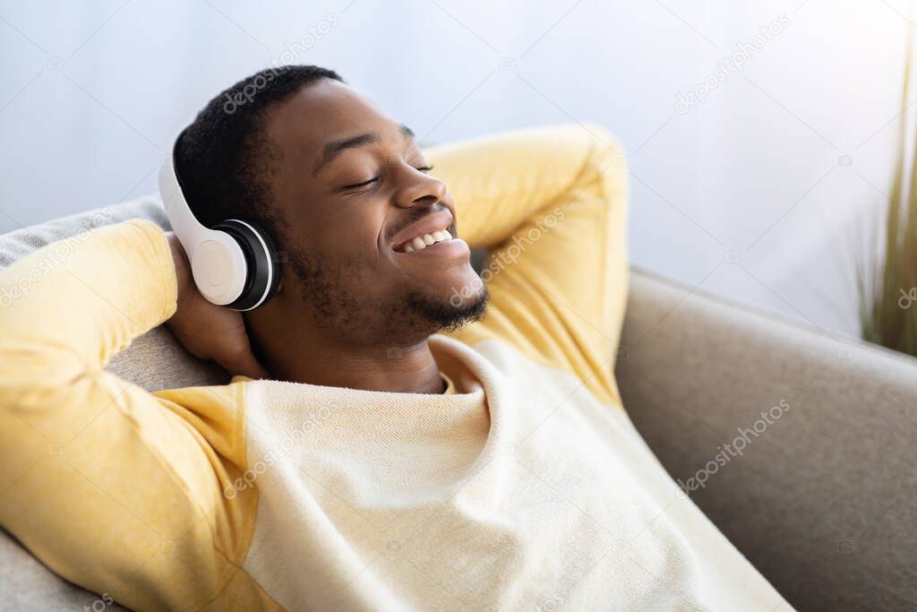 Closeup of relaxed black guy listening to music, using headset