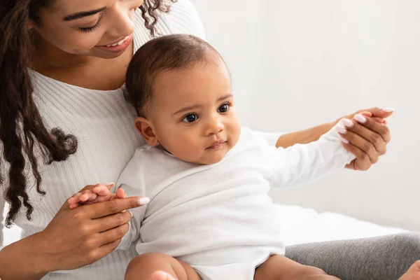 African Mom Cuddling Playing With Adorable Little Baby In Bedroom