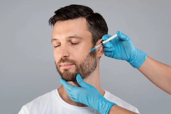 Atraktivní muž středního věku dostává anti-aging proceduru, šedé pozadí — Stock fotografie