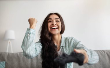 Online video oyunu oynayan mutlu Hintli kadın, evde EVET hareketi yapıyor