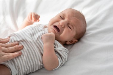 Closeup Portrait Of Crying Little Newborn Baby In Bodysuit Lying On Bed clipart