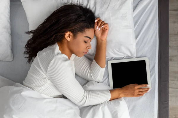 Mujer negra acostada en la cama, durmiendo y sosteniendo la tableta —  Fotos de Stock