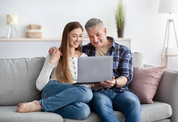 Feliz casal maduro sentado no sofá com computador portátil, conversando com amigo ou família on-line, dentro de casa — Fotografia de Stock
