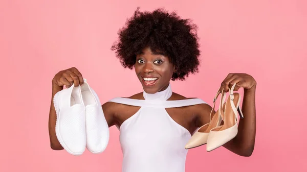 Mujer negra eligiendo calzado entre zapatillas de deporte y tacones altos, fondo rosa —  Fotos de Stock