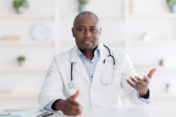 Hastalar tıbbi konsültasyona bakıyorlar. Siyah erkek doktor ofisinde kameraya işaret ediyor. — Stok fotoğraf
