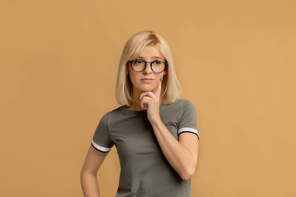 Mujer pensativa en gafas pensando en la pregunta, tocando la barbilla y mirando hacia otro lado, fondo beige —  Fotos de Stock