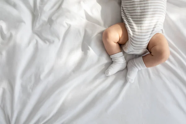 Vista superior del bebé recién nacido en traje de cuerpo y calcetines acostado en la cama —  Fotos de Stock