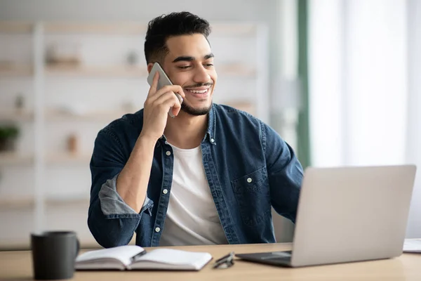 Middle-eastern man working online, using laptop and mobile phone