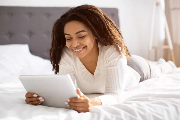 Mujer negra feliz acostada en la cama usando tableta — Foto de Stock