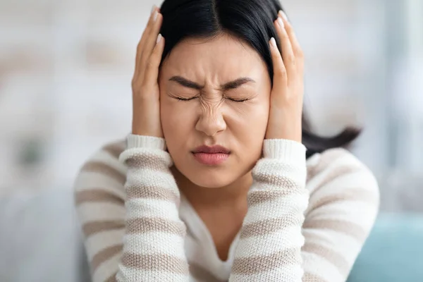 Emotionale Asiatin, die zu Hause Ohren mit Händen bedeckt — Stockfoto