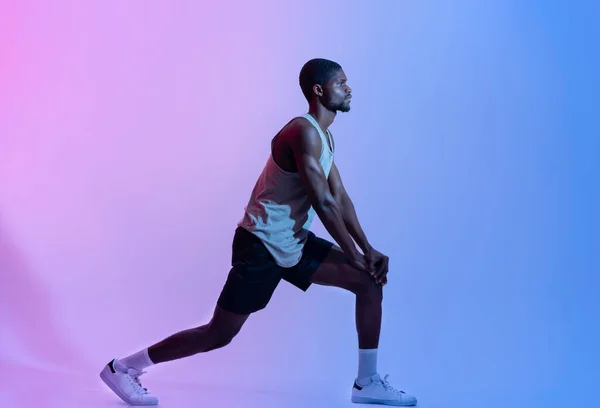 Πλευρική άποψη του ταιριαστού μαύρου άνδρα στα αθλητικά να κάνει lunges σε νέον φως, ολόσωμο πορτραίτο. Υγιής έννοια διαβίωσης — Φωτογραφία Αρχείου