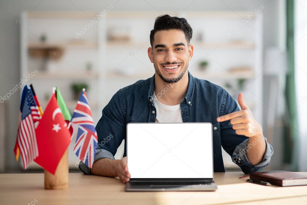 Happy arab guy pointing at laptop with empty screen