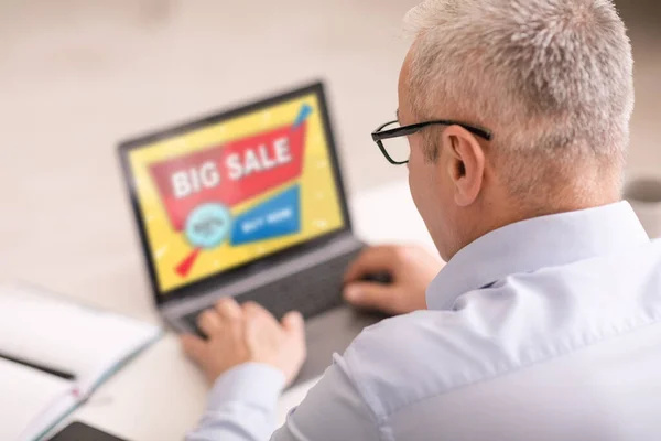 Elderly man purchasing online, using laptop at home