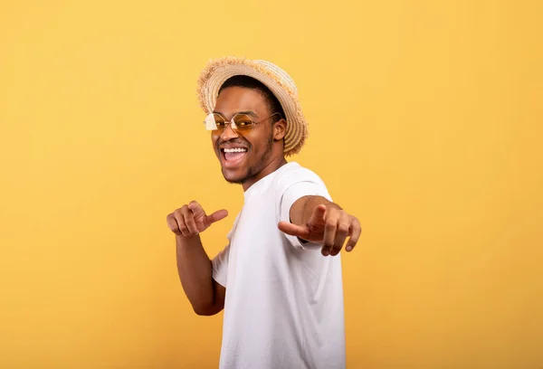 Cara preto feliz em roupa de verão casual, chapéu de palha e óculos de sol apontando para você no fundo do estúdio amarelo — Fotografia de Stock