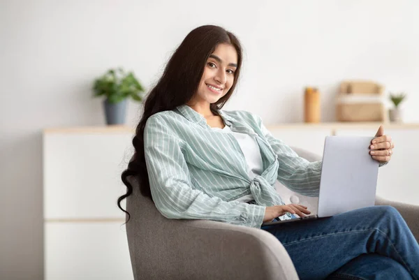 Gelukkig Indiase dame zitten in fauteuil met moderne laptop, studeren op afstand of het hebben van zakelijke bijeenkomst thuis — Stockfoto