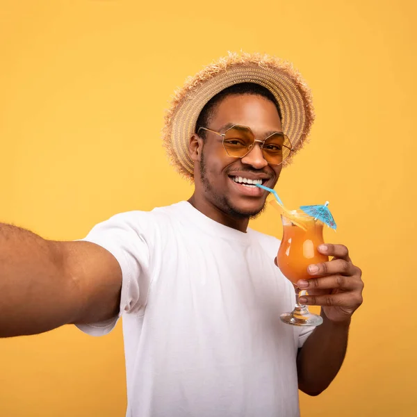 Snygg svart kille i sommar outfit dricka exotiska cocktail och ta selfie på gul studio bakgrund — Stockfoto