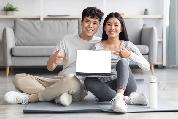 Happy sporty asian couple showing laptop with blank screen