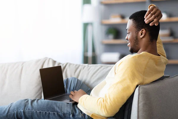 Ontspannen zwarte man met behulp van laptop met leeg scherm, interieur — Stockfoto