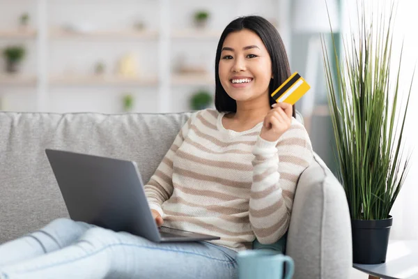 Banca en línea. Mujer asiática feliz con el ordenador portátil y tarjeta de crédito en casa — Foto de Stock